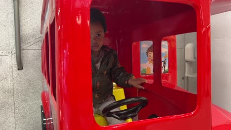 exótico bebé negro de dos años, mezcla de carreras, montando en un gran autobús de juguete rojo