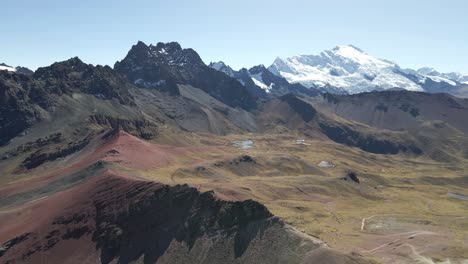 Drone-advances,-showcasing-Rainbow-Mountain-against-a-backdrop-of-snowy-Ausangate-peaks