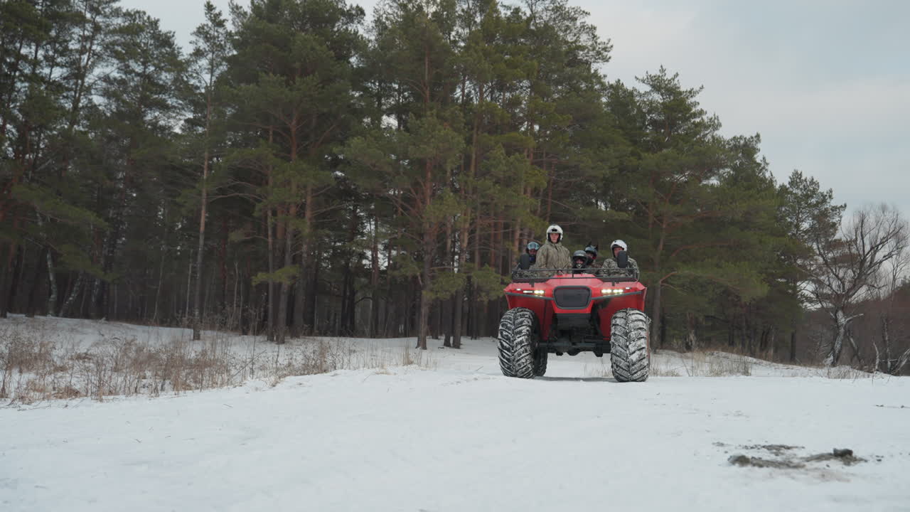 Ampia inquadratura di un ATV rosso nella neve, due piloti esplorano un campo innevato aperto verso il limite della pineta, a passo costante con tracce di pneumatici visibili, sotto un cielo terso, un'atmosfera di lavoro di squadra ed esplorazione, con la luce del mattino e un approccio misurato.