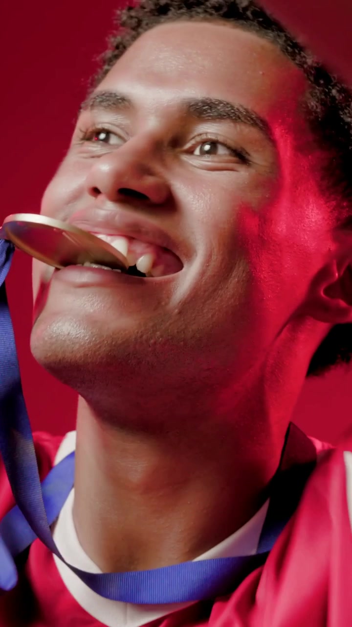 Vertical video: Camera zooming out, male cheering and biting medal in red jersey studio, copy space