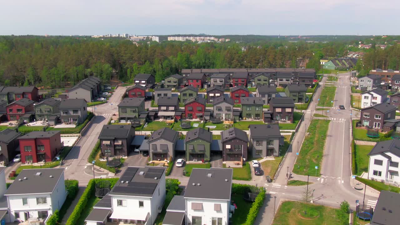 Široký paralaxní záběr dronem na hustě zastavěnou novou obytnou zástavbu s různými barvami domů a dobře naplánovanými ulicemi
