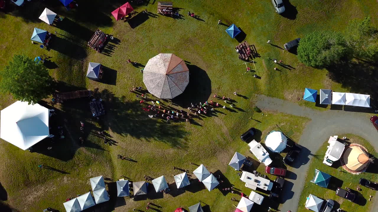Bird"s-eye view of a Powwow event. Tents are set in a circular pattern. The drone shot rotates by following the pattern.