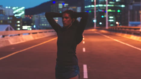 woman stretching on a city bridge at night