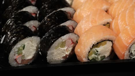 los rollos de sushi giran en un recipiente de plástico sobre un fondo negro. entrega de comidas