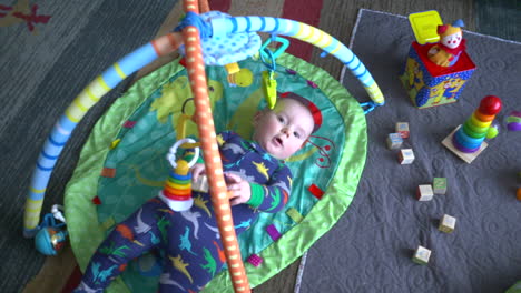 top down shot of a cute baby boy actively playing with toys in a baby gym