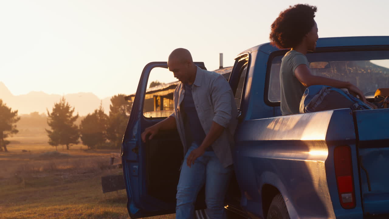 Coppia che scarica lo zaino da un pick-up durante un viaggio on the road verso una baita in campagna