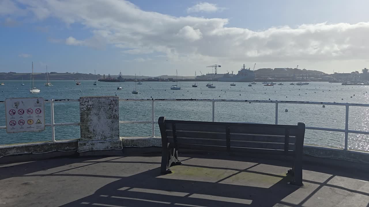 Wooden Bench on Pier Overlooking Falmouth Estuary Toward Naval Dockyard on a Sunny Day in Cornwall England