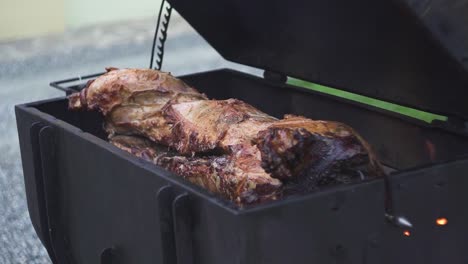 barbecuing a juicy pig in a black metal grill outdoors, slow motion