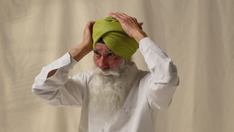 studio shot of senior sikh man with beard tying fabric for turban against plain background 4