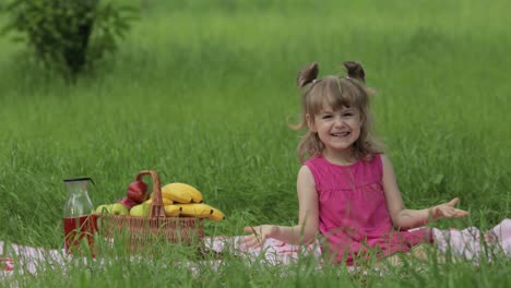 Weekend-at-picnic.-Lovely-caucasian-child-girl-on-green-grass-meadow-sit-on-blanket-waving-her-hands