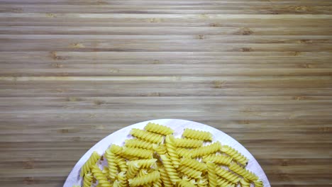 01:05 - pasta de fusilli cruda girando sobre una tabla de cortar en blanco, en bucle