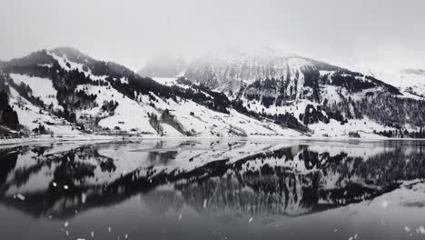 el paisaje montañoso nevado se refleja en el agua clara del lago durante las nevadas, vista aérea de drones