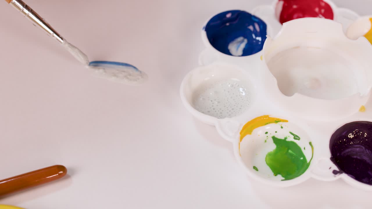 Mani che mescolano colori ad acquerello su palette con pennello, illuminazione intensa, vista dall'alto, area di lavoro creativa