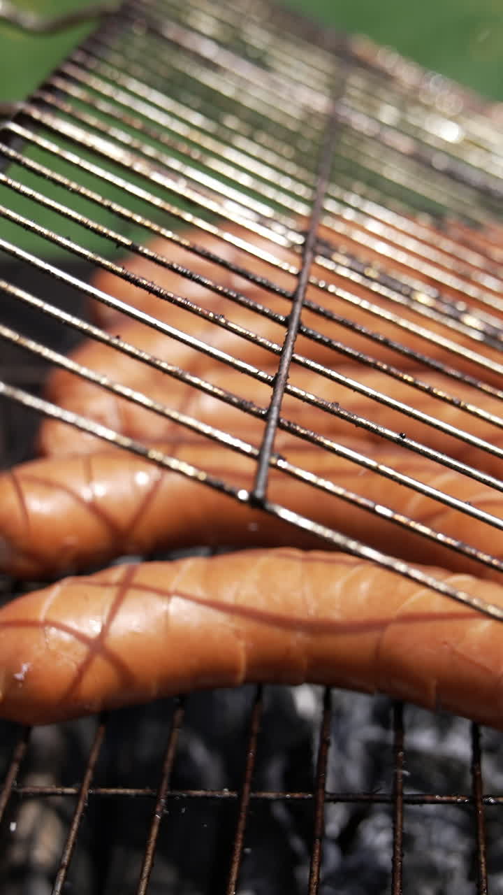 Man putting sausages on the grill. Grilled fresh meat sausages on an open air. Ruddy sausages are fried on charcoal. Close-up. Vertical video