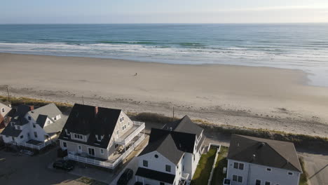 aerial fly over of houses leading to beach with lone person walking with dog