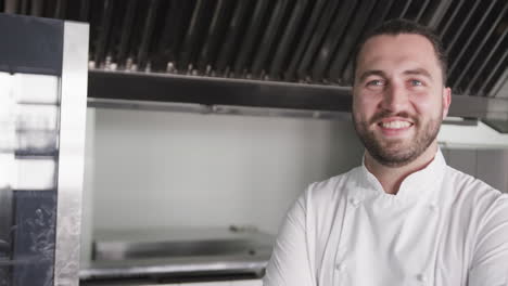 Portrait-of-happy-caucasian-male-chef-with-beard-smiling-in-kitchen,-copy-space,-slow-motion