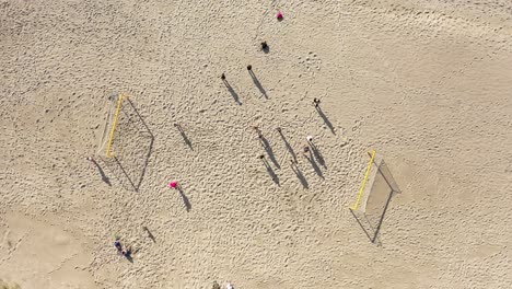 Antenne:-Rotierende-Aufnahme-Von-Menschen,-Die-Auf-Einem-Fußballplatz-Stehen,-Mit-Langen-Schatten-Auf-Sand