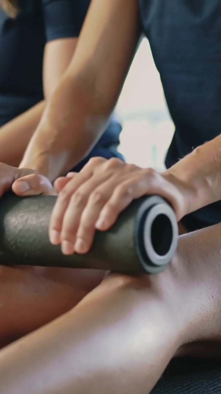 Vídeo vertical: Casal de preto usando rolo de espuma nas coxas em casa, pós-treino, para alívio.