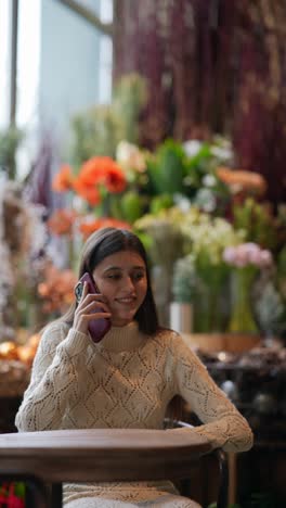 una mujer joven hablando por teléfono en una floristería.