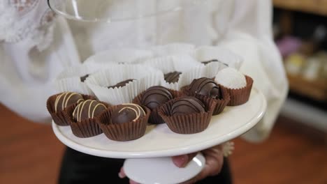 close-up of a woman holding chocolate candies or pralines on a tray.