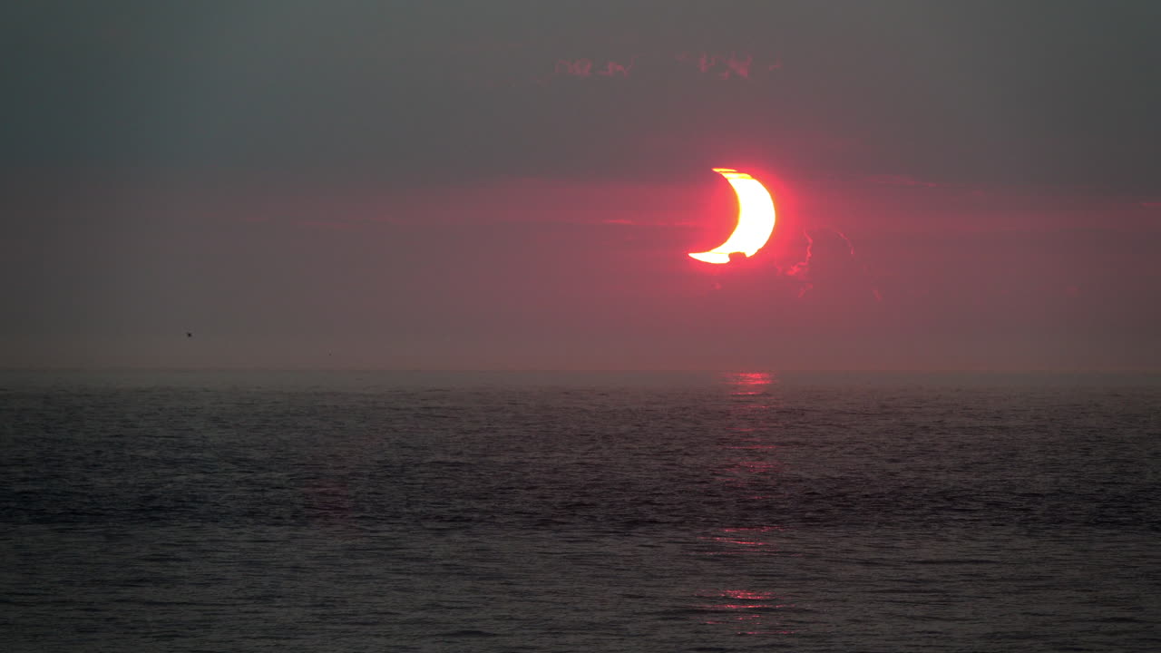 sol en forma de media luna al amanecer, durante un eclipse solar parcial, se eleva sobre el océano