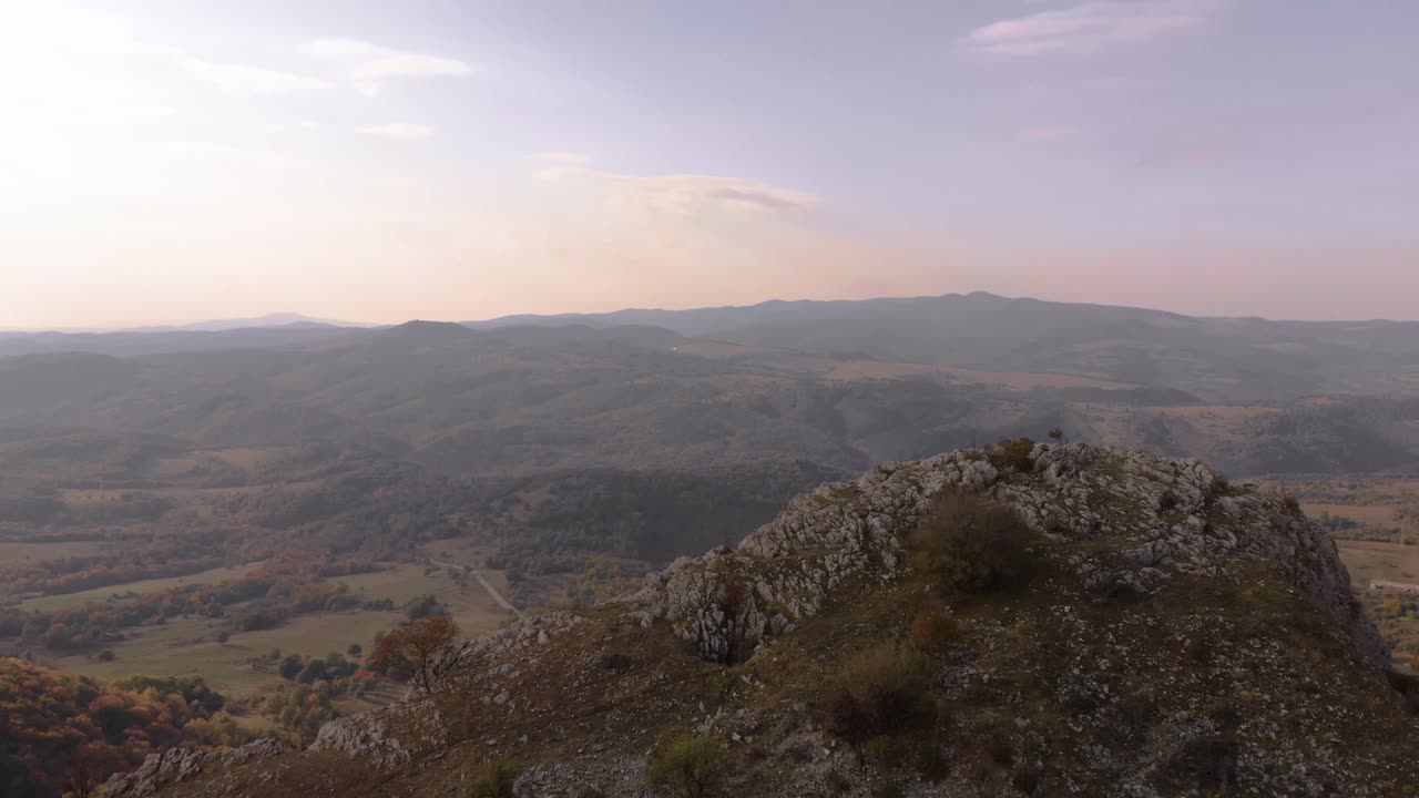 Ripresa aerea in allontanamento sopra una collina rocciosa, una valle e una foresta come sfondo
