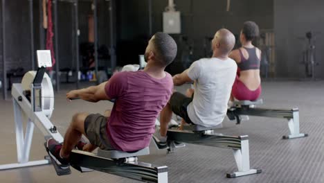 Rear-view-of-diverse-group-fitness-class-training-hard-on-rowing-machines-at-gym,-in-slow-motion