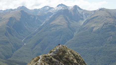 people walking through a moutain range with mountains behind them at the brewster track in mount aspiring national park, new zealand