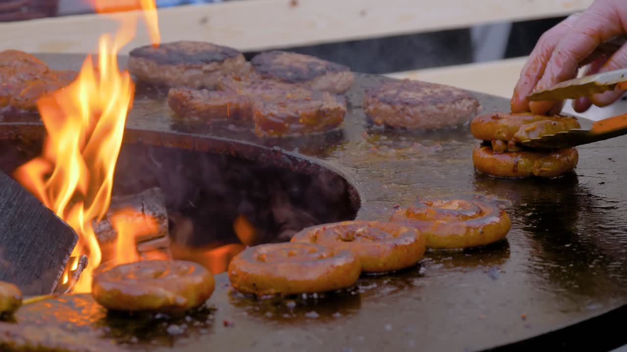 느린 동작: 셰프가 뜨거운 불꽃으로 브레이저에 신선한 나선형 돼지고기 소시지를 그릴 때