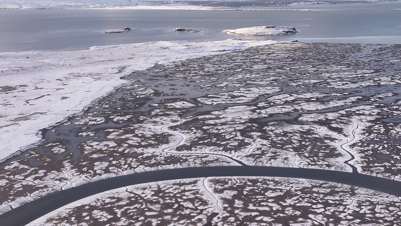 Aerial drone zoom in to Borgarfjörður, Iceland’s snow-covered landscape, icy coastline, islands and mountain.