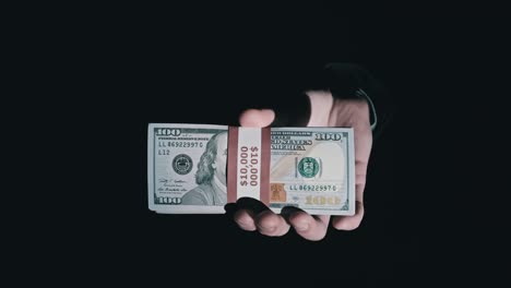 una pila de 10.000 dólares estadounidenses en paquetes en manos masculinas sobre un fondo negro.