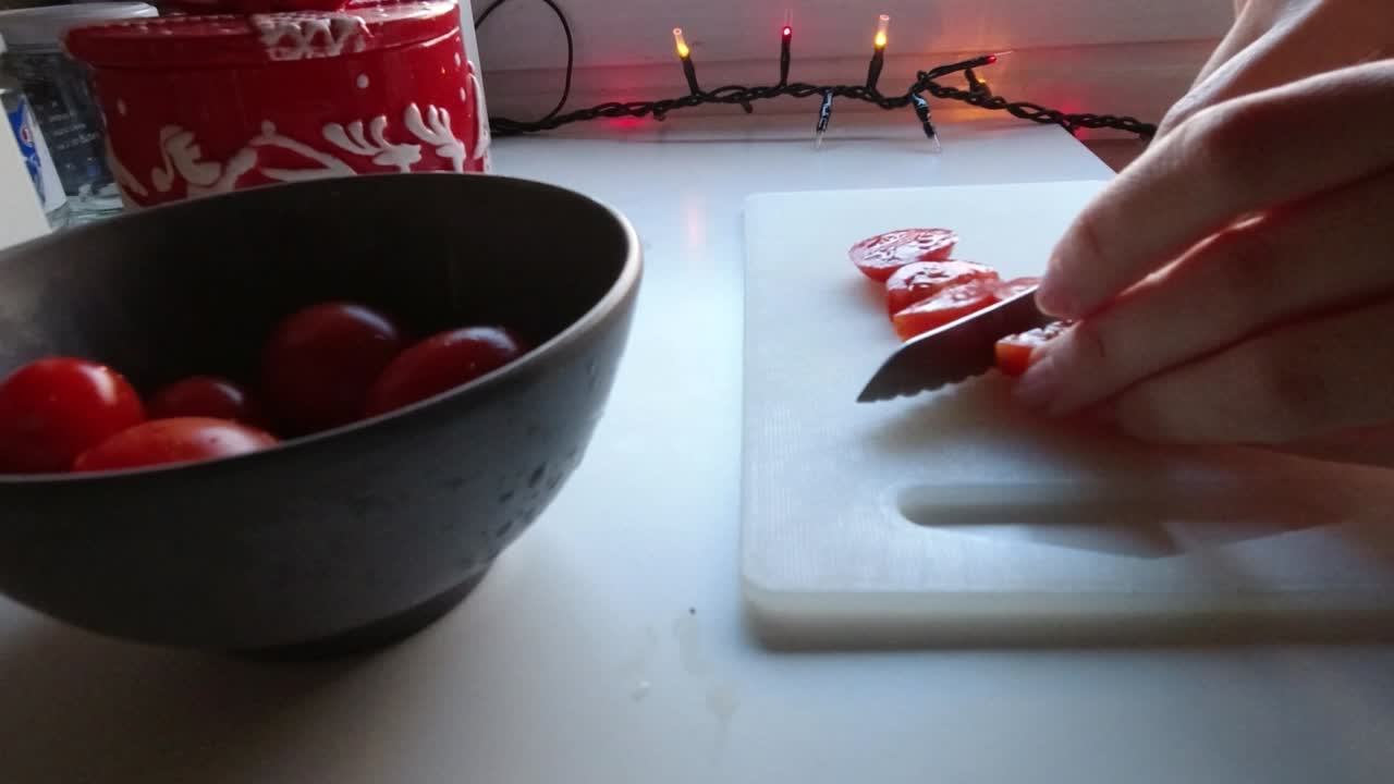 Slicing some cherry tomatoes in the christmas decorated kitchen near the window. Steady camera shot.