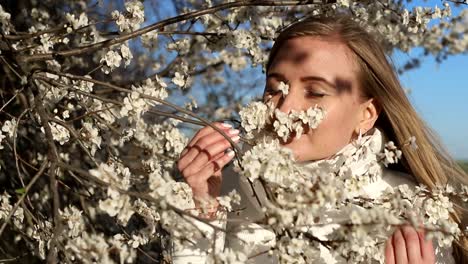 girl in white jacket photographs white color in spring using smartphone for photo blonde girl in a white mask makes a selfie on a background of flowering fruit trees photos for social networks