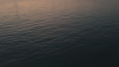 AERIAL:-Slow-Tilt-up-over-East-River-Waves-showing-Manhattan-New-York-City-Skyline-in-Beautiful-Dawn-Sunset-Orange-Light