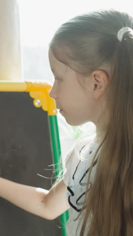 schoolgirl with long pigtails writes mathematical problems with chalk on chalkboard slow motion. girl studies arithmetic. lesson in primary school