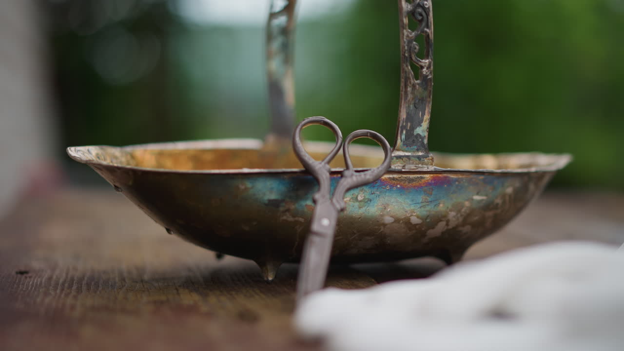 Old scissors closeup. Detailed shot of aged scissors resting on brass vessel with garden backdrop. Focused photograph capturing old scissors leaning on brass container amidst blurred garden scene