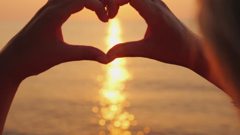 female hands show the shape of the heart above the sea where the sun rises beautiful romantic scene