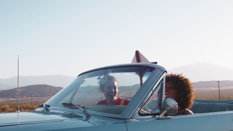 laughing female friends driving in convertible on a highway