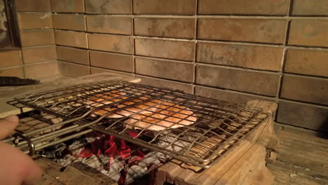 handheld shot of man closing grilling basket with seasoned chicken inside and flipping on charcoal bbq at night