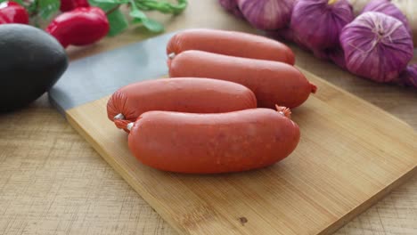 raw sausages on wooden cutting board with garlic and vegetables