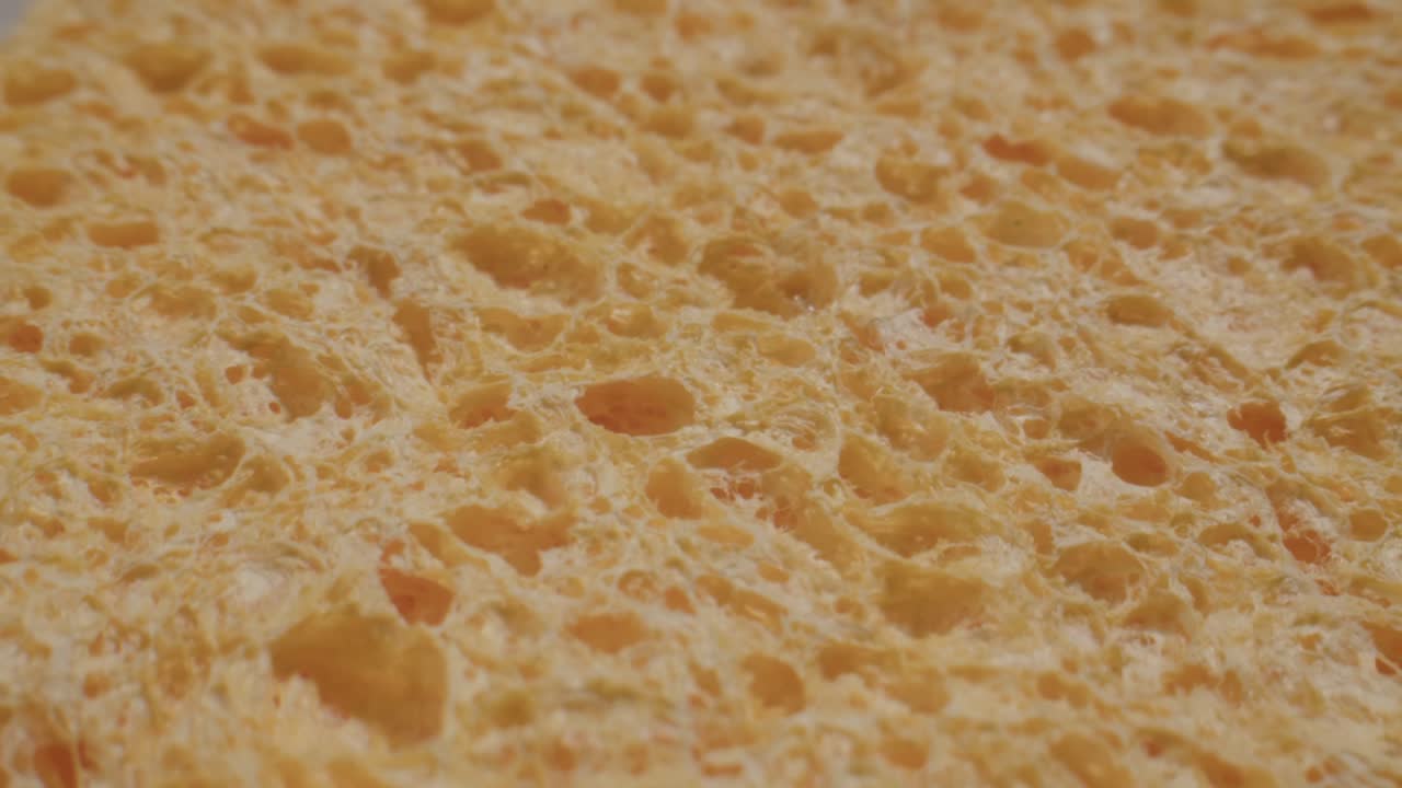 Close-up Macro Shot of Porous Yellow Sponge Absorbing Water