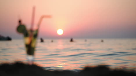 People-in-sea-and-cocktail-on-beach-at-sunset