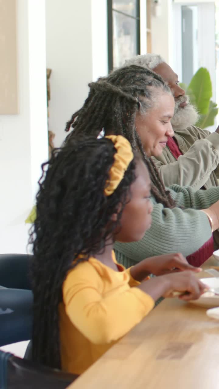 Vertical video: Lifting grandpa offering bottle at table, child in yellow top eating tomatoes