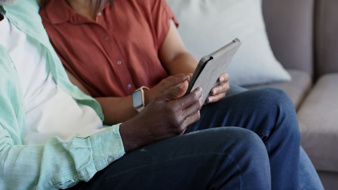Due adulti sono seduti sul divano, la persona a sinistra tocca e poi scorre il tablet per navigare i contenuti.
