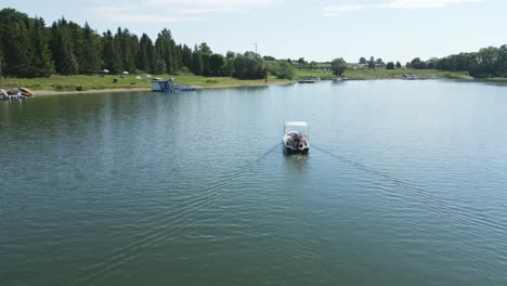 Camera-passes-over-a-small-motorboat-sailing-into-a-bay-with-anchored-sailboats-and-a-small-grassy-beach