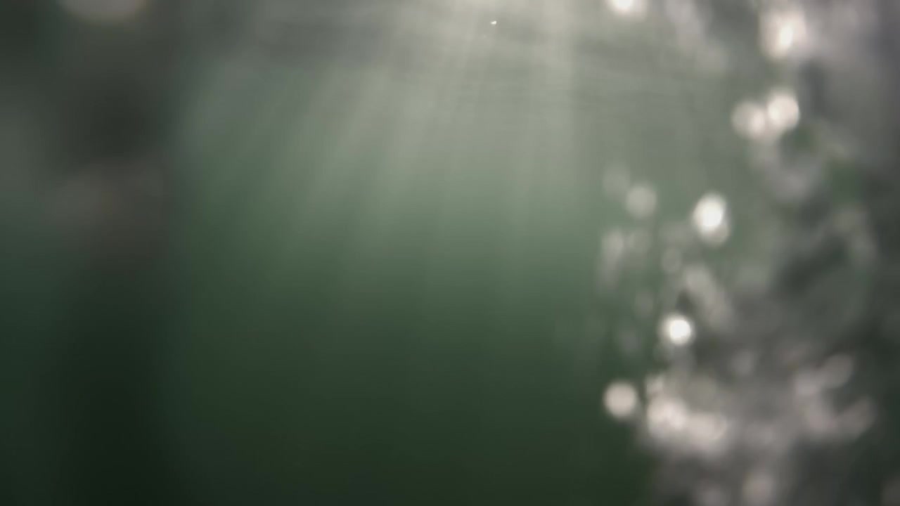 Abstract view of water splashing against a bright light source, creating shimmering bokeh and refreshing liquid movement