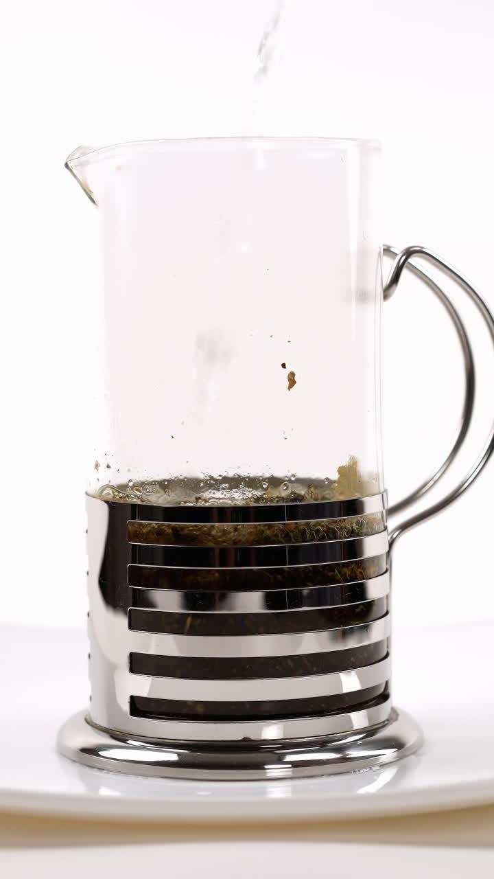 verter agua caliente en una prensa francesa con hojas de té en un plato blanco, proceso de elaboración de la cerveza