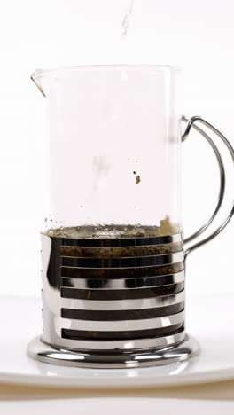 verter agua caliente en una prensa francesa con hojas de té en un plato blanco, proceso de elaboración de la cerveza