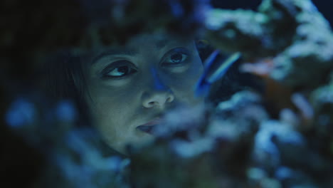 woman looking at colorful fish in aquarium tank watching colorful sea life swimming in corel reef observing marine ecosystem