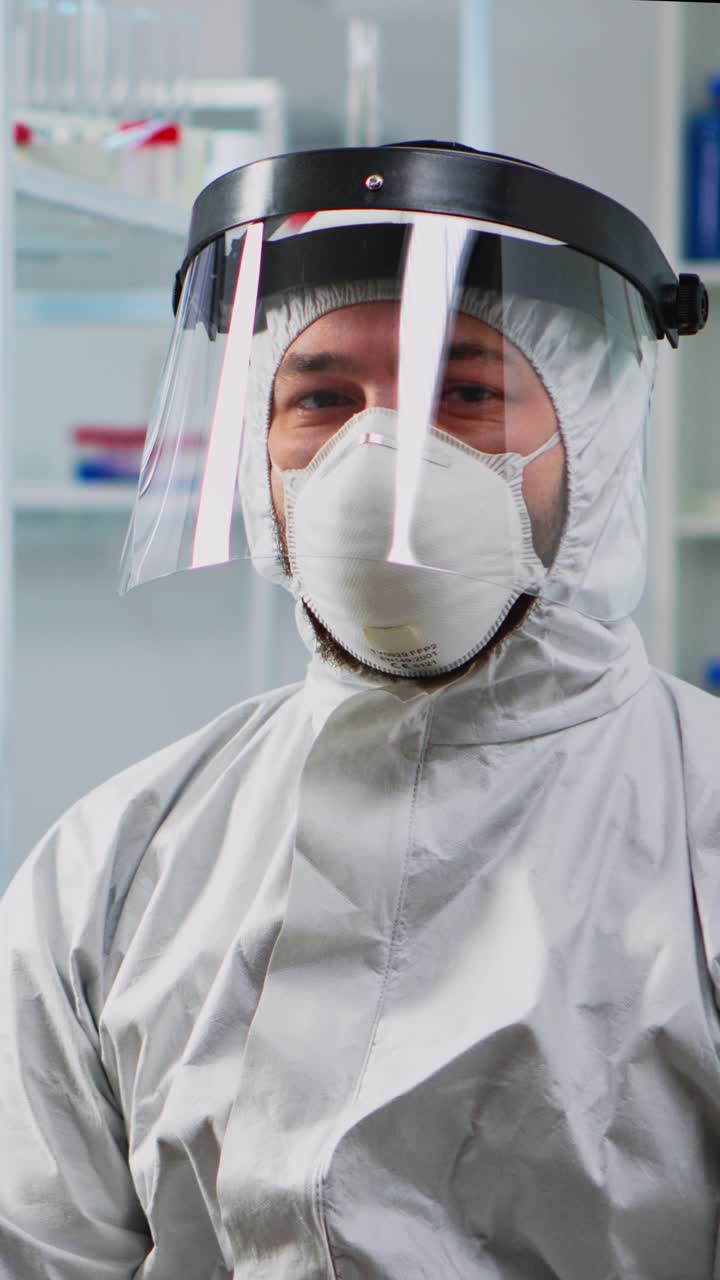 Vertical video: Doctor in protection suit looking exhausted at camera
